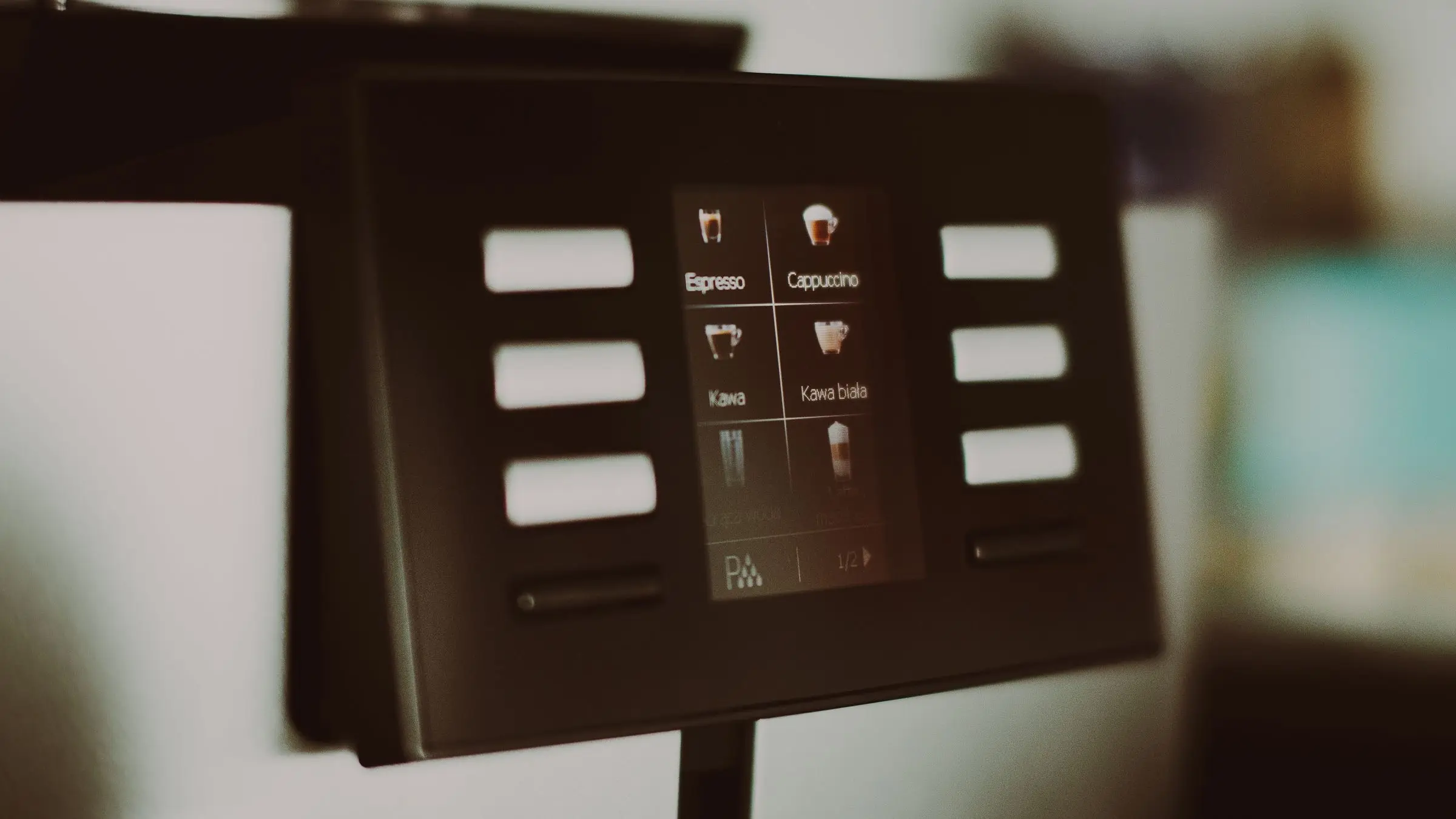 A coffee machine touchscreen on a stalk showing four drink choices with small cup icons.