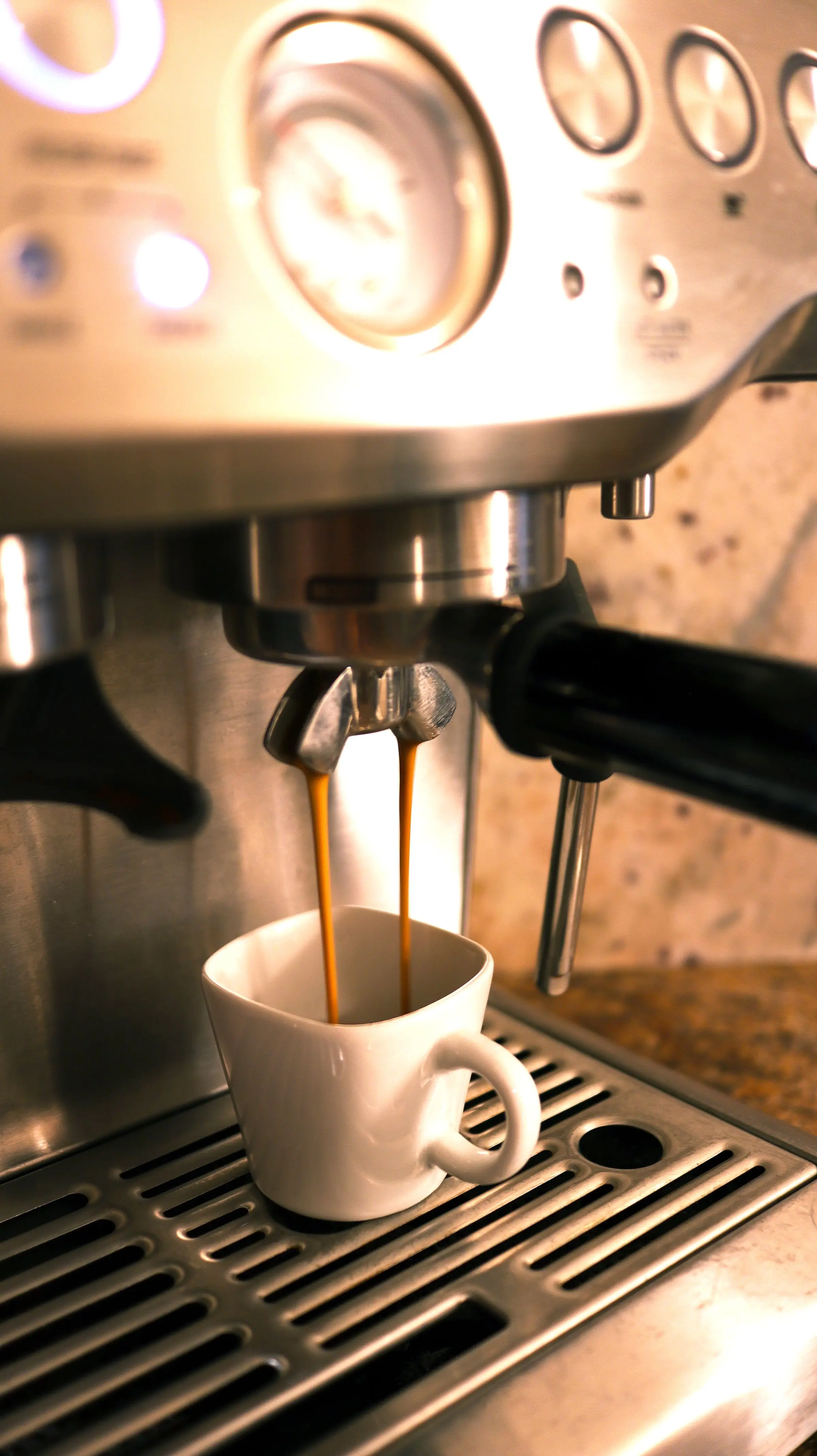 Two streams of espresso running from a portafilter into a small white cup on a stainless steel drip tray.